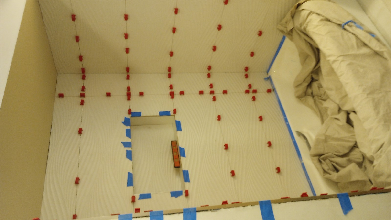 Tile installation in progress with red leveling clips on cream porcelain wood-grain large-format tile